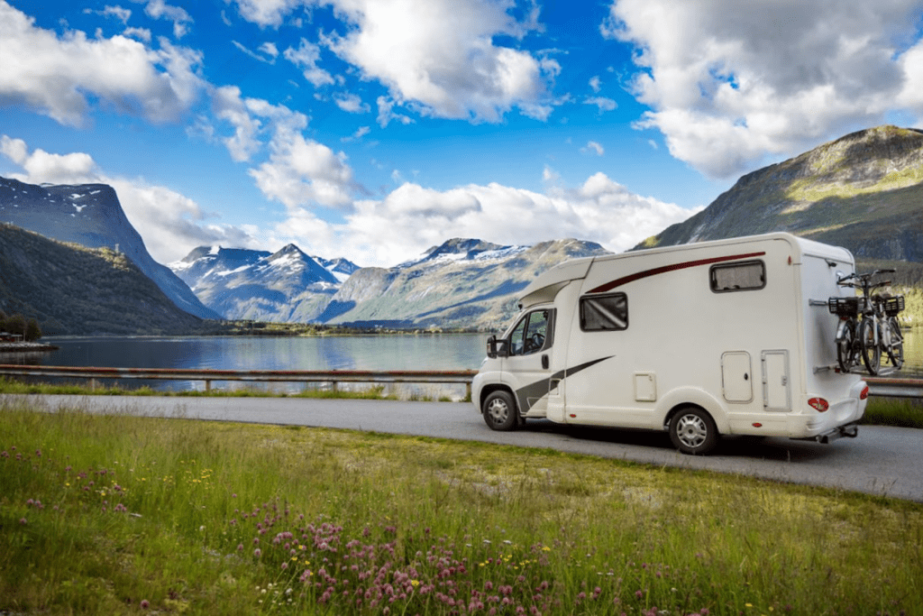 Scenic view featuring a parked camper van by a serene lake, surrounded by mountains, promoting outdoor adventure and travel.